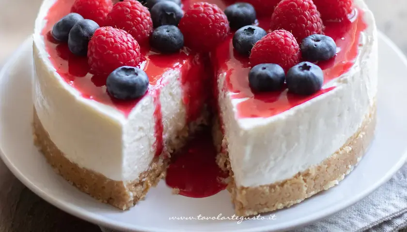 Delizioso cheesecake con mascarpone, guarnito con lamponi freschi, mirtilli e una colata di salsa rossa.