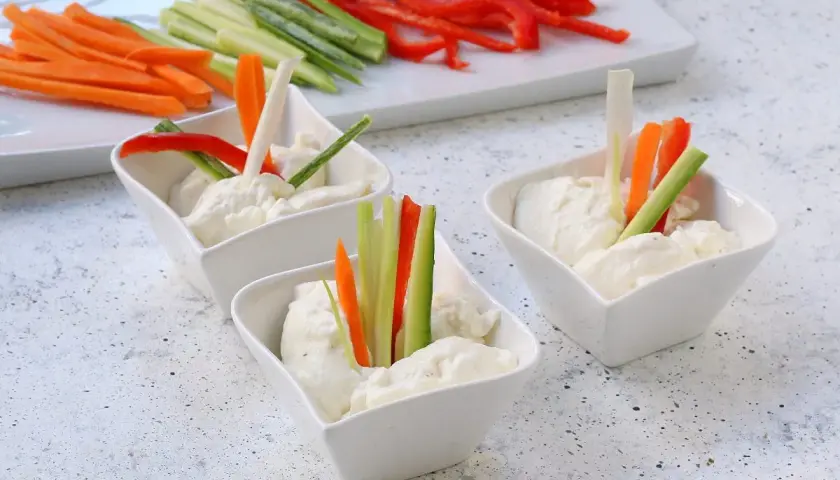 Tre ciotoline con mousse di caprino e bastoncini di verdure fresche: carote, cetrioli e peperoni rossi.