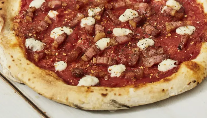 Pizza con guanciale croccante, pomodoro e fiocchi di pecorino, un sapore intenso e autentico.