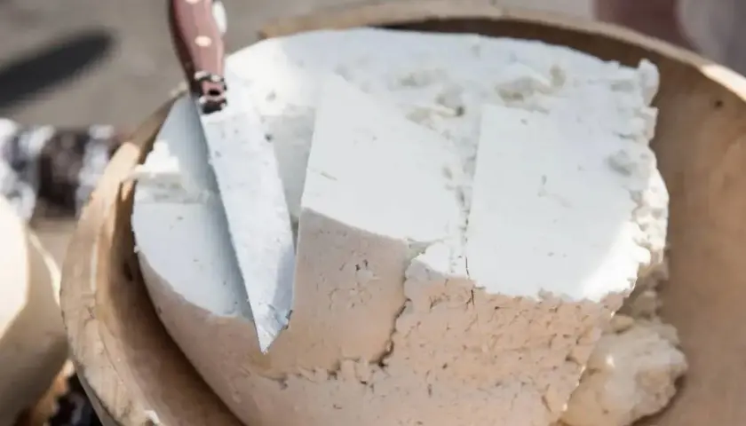 Formaggio fresco e morbido, simile a uno stracchino, tagliato in una ciotola di legno con un coltello.