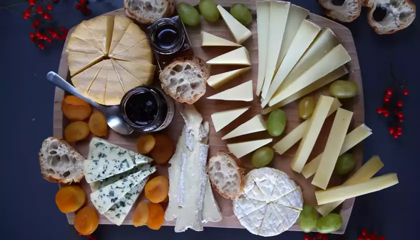 Un tagliere ricco di formaggio di capra francese, accompagnato da pane croccante, uva, albicocche secche e marmellata.