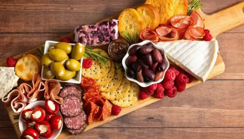 Tagliere ricco di antipasti sfiziosi: salumi, formaggi, olive, lamponi e crostini. Un tripudio di sapori e colori.