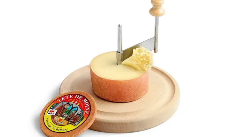 Forme di formaggio Tête de Moine su tagliere di legno, con girolle per creare riccioli.