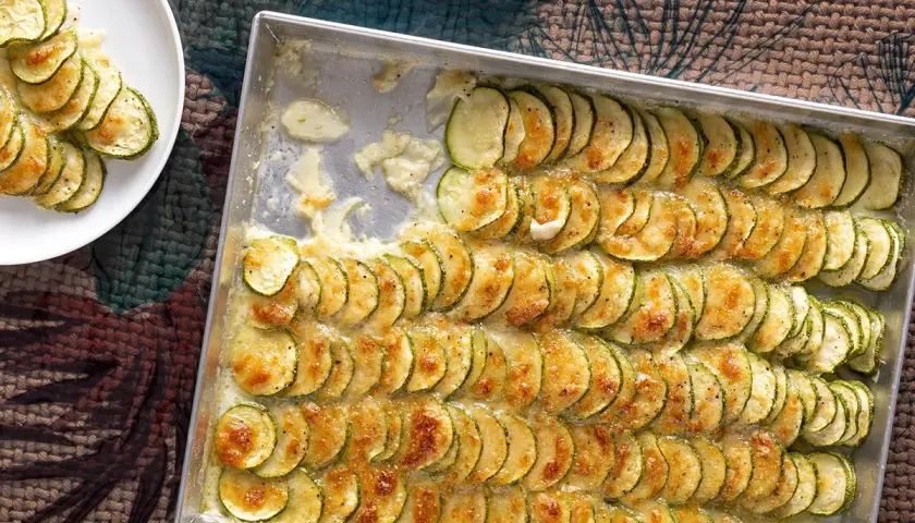 Zucchine al forno con mozzarella, disposte a raggiera in una teglia, dorate e filanti. Un piatto semplice e gustoso.