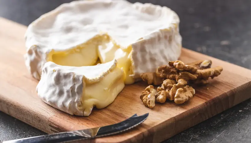 Un pezzo di brie, un formaggio grasso, su un tagliere con noci e un coltello.
