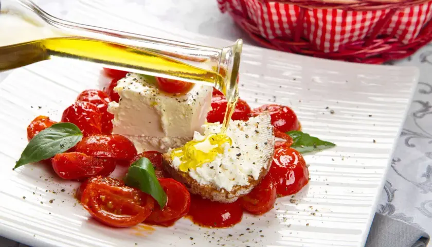 Un piatto di pomodorini confit con robiola, perfetto per un pasto leggero e nutriente in gravidanza. Olio d'oliva versato su una fetta di pane con formaggio.