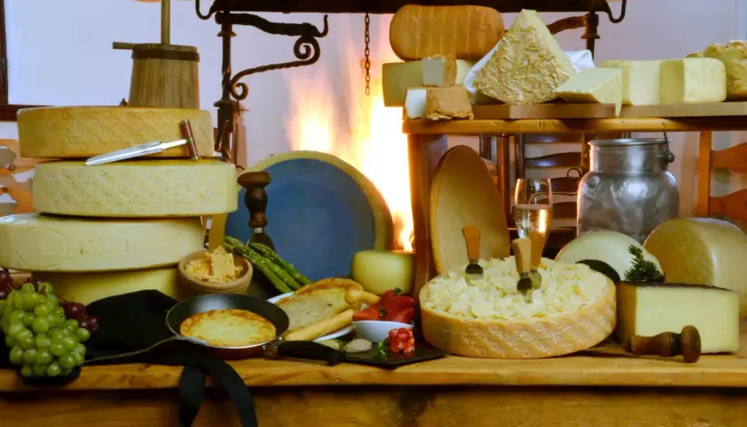 Varietà di formaggi pasta semidura, tra cui forme intere e pezzi tagliati, con uva, fragole e una padella con tortino.