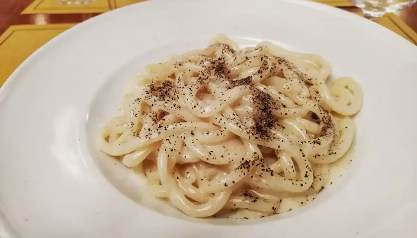 Pici cacio e pepe cremosi e fumanti, un classico della cucina romana, serviti su un piatto bianco.