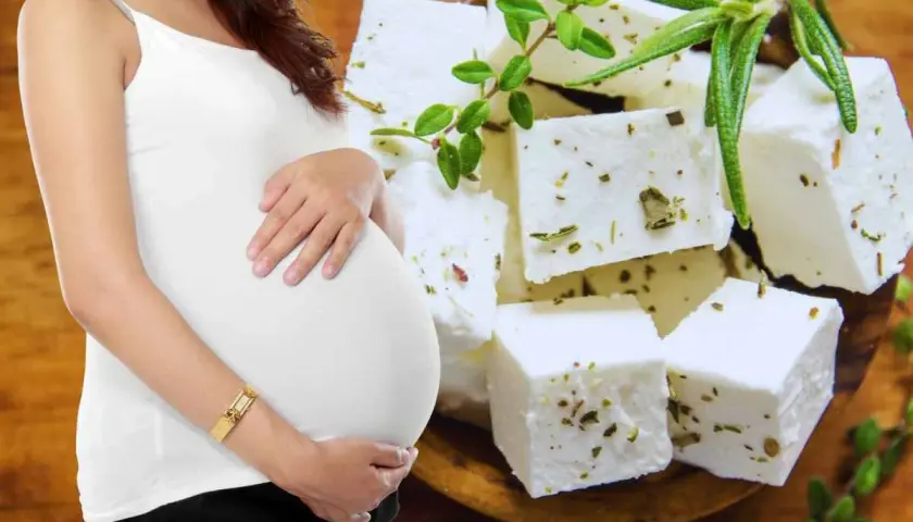 Pancia di donna incinta accarezzata, con cubetti di feta aromatizzata alle erbe sullo sfondo.