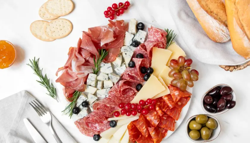 Un invitante piatto di formaggi con salumi, uva, olive e pane croccante, perfetto per un aperitivo.