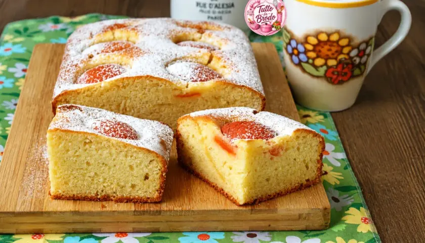 Torta albicocche e yogurt soffice, cosparsa di zucchero a velo, con pezzi di albicocca visibili. Perfetta per la colazione.