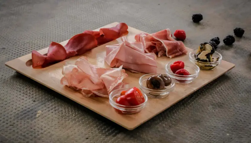 Un invitante tagliere di antipasti con salumi, olive, pomodorini e frutti di bosco, pronto per essere gustato.
