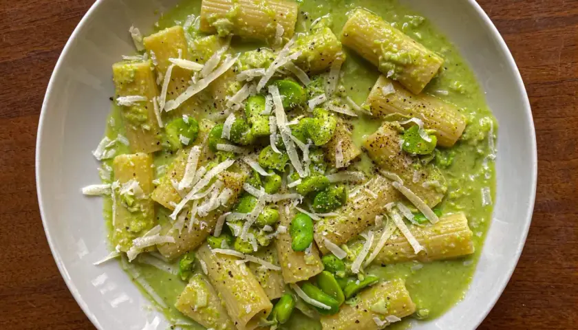 Piatto di pasta con fave fresche, crema verde e scaglie di pecorino. Un primo piatto primaverile invitante.