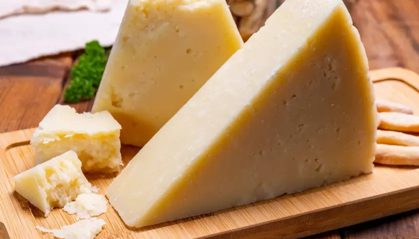Fette di pecorino stagionato su tagliere di legno, con briciole e grissini sullo sfondo.