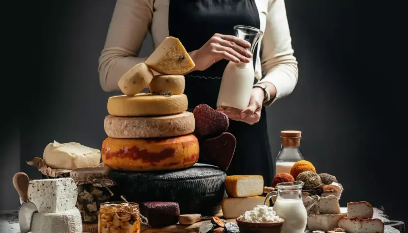 Una ricca selezione di formaggio a latte crudo, tra cui forme rotonde e quadrate, con latte fresco in caraffa.