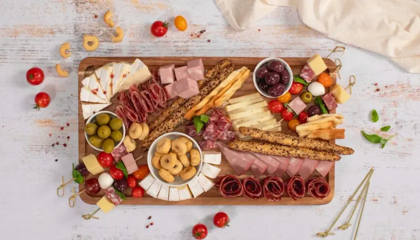 Un ricco antipasto salumi e formaggi su tagliere: salame, prosciutto, brie, taralli, olive e pomodorini.