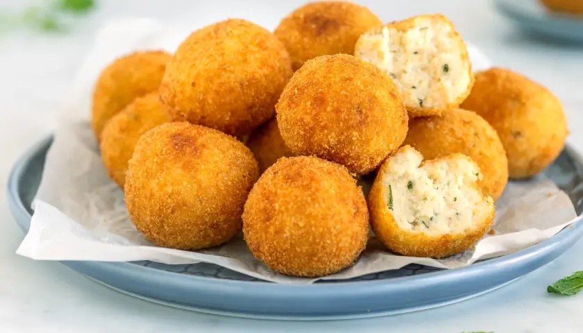 Arancini dorati e croccanti, perfetti per gustose ricette con ricotta. Uno è morso, rivelando un ripieno morbido e saporito.