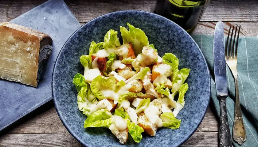 Insalata Caesar con crostini e una generosa spolverata di crema di pecorino. Accanto, un pezzo di formaggio stagionato.