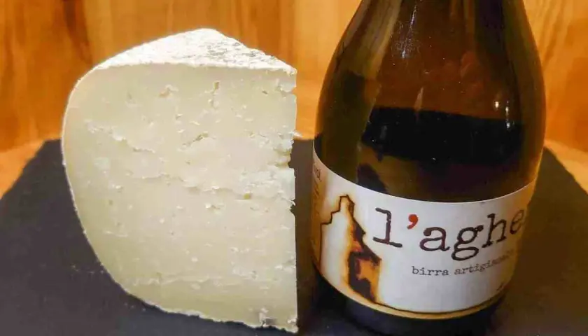 Un pezzo di formaggio stagionato accanto a una bottiglia di birra artigianale. Un abbinamento perfetto di birra e formaggio.