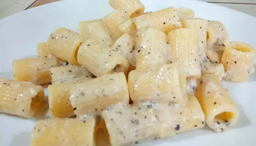 Un piatto di pasta cacio e pepe, con rigatoni cremosi e pepe nero macinato.