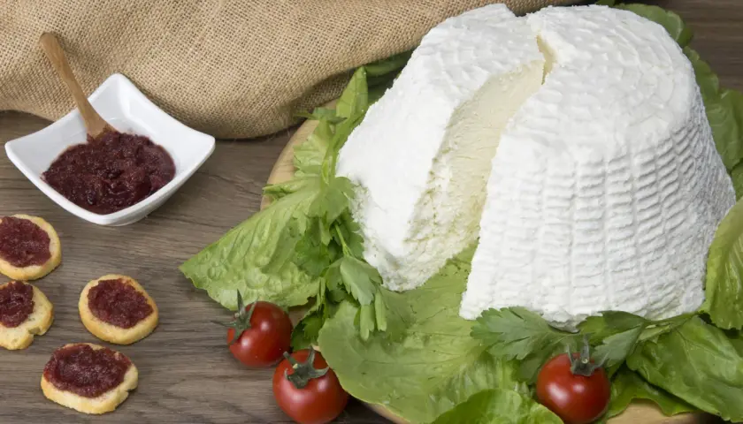 Un grande blocco di ricotta fresca, circondato da lattuga e pomodorini, con bruschette e marmellata in una ciotola. Diversi tipi di ricotta sono presentati in modo invitante.