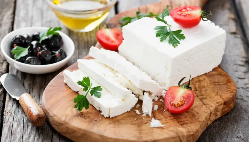 Una porzione feta fresca, tagliata a fette, con pomodorini e olive nere su un tagliere di legno.