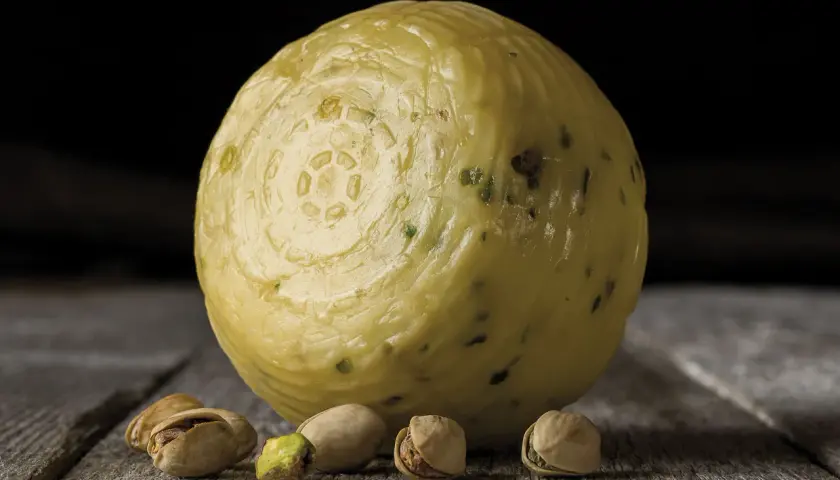 Formaggio pecorino al pistacchio, con alcuni pistacchi sparsi sul tavolo di legno.