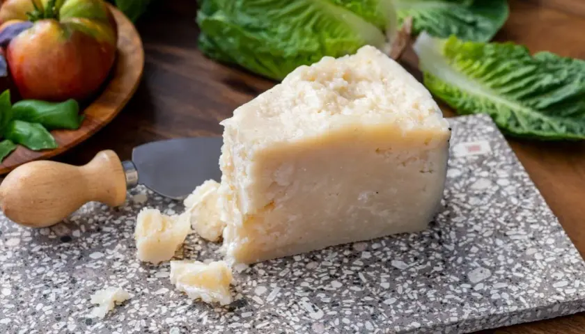 Un pezzo di pecorino siciliano stagionato, pronto per essere gustato con pomodori e lattuga fresca.