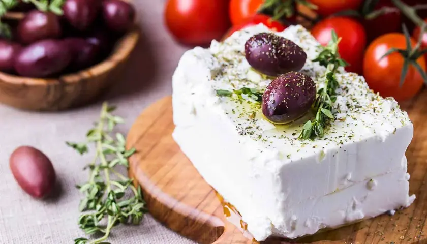 Blocco di feta condito con olive e erbe aromatiche, perfetto per scoprire quante calorie ha la feta in una gustosa insalata greca.