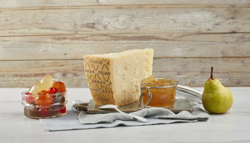 Un pezzo di Grana Padano stagionato, un vasetto di miele dorato e frutta candita, pronti per un abbinamento delizioso.
