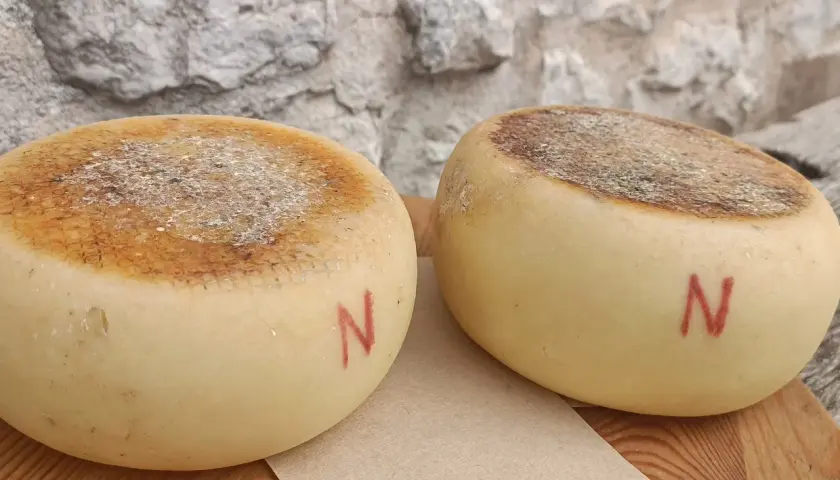 Due forme di pecorino semistagionato, con la crosta marcata e la lettera "N" rossa dipinta sul fianco, riposano su un tagliere di legno.