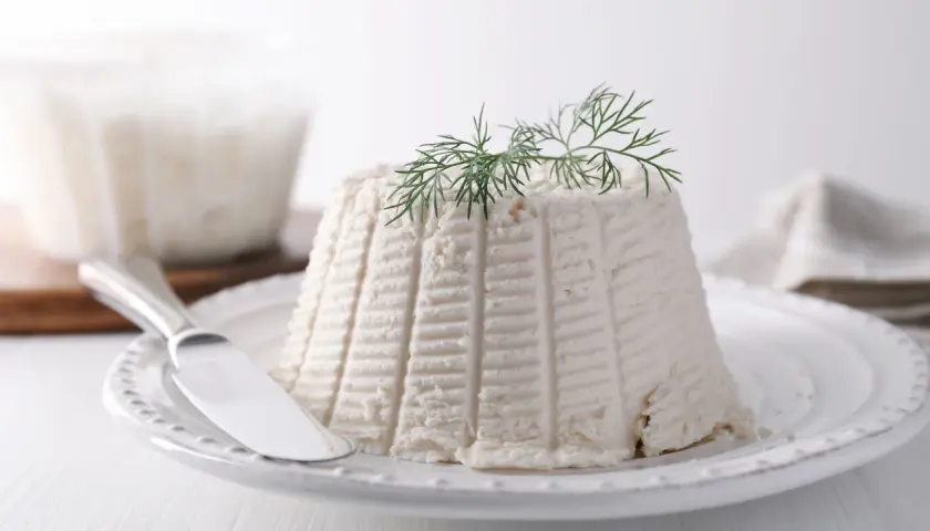 Ricotta fresca su piatto bianco, guarnita con aneto. La sua consistenza soffice rivela cosa contiene la ricotta: pura bontà.