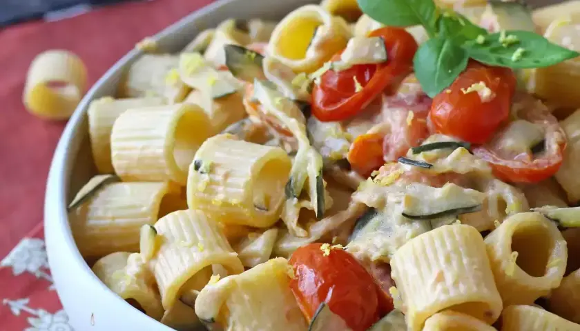 Piatto cremoso di pasta con zucchine, pomodorini e Philadelphia, guarnito con basilico fresco.