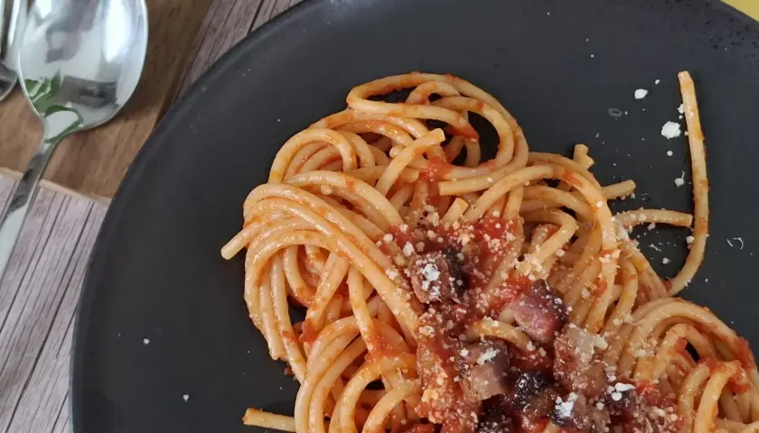 Un piatto di pasta all'amatriciana fumante, con guanciale croccante e pecorino grattugiato, pronto per essere gustato.