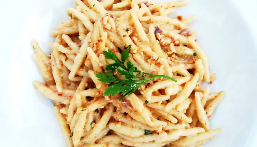Un piatto di trofie cacio e pepe, condite con una cremosa salsa al formaggio e pepe, guarnite con prezzemolo fresco.