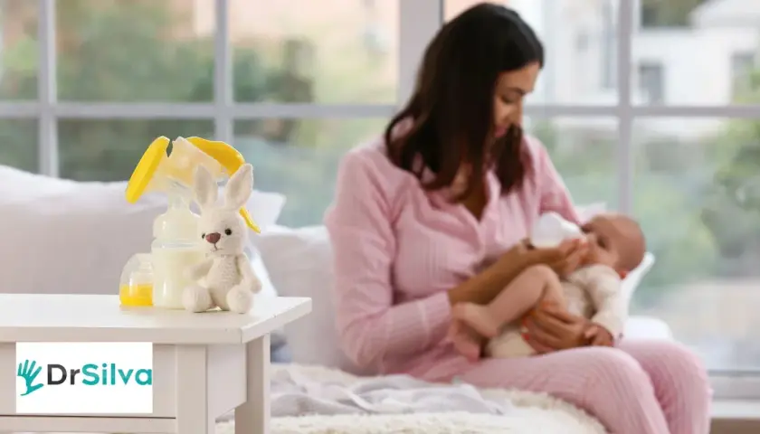 Mamma nutre il neonato con il biberon. Sul tavolino, un coniglietto di peluche e accessori per la pappa, come i latticini e derivati.