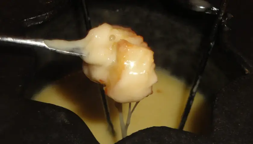 Un pezzo di pane intinto nella fonduta savoyarde ricetta, filante e dorato, pronto per essere gustato.