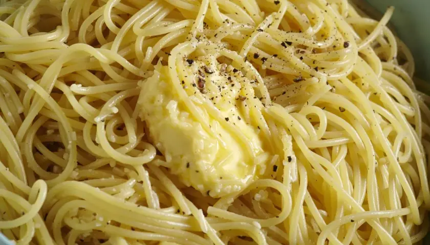 Un piatto di spaghetti fumanti, conditi con burro fuso e pepe nero macinato, pronti per essere gustati come un classico cacio e pepe.