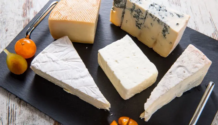 Assortimento di formaggi, tra cui un cremoso formaggio morbido, un erborinato e altri tipi, guarniti con frutta.