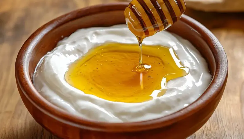 Un cucchiaio di miele cola su uno yogurt cremoso in una ciotola di legno. Attenzione, yogurt e miele fa ingrassare se consumati in eccesso!
