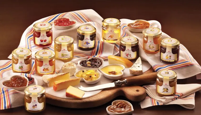 Una selezione di conserve, tra cui composta di fichi per formaggi, salse dolci e confetture, disposte su un tagliere con formaggi.