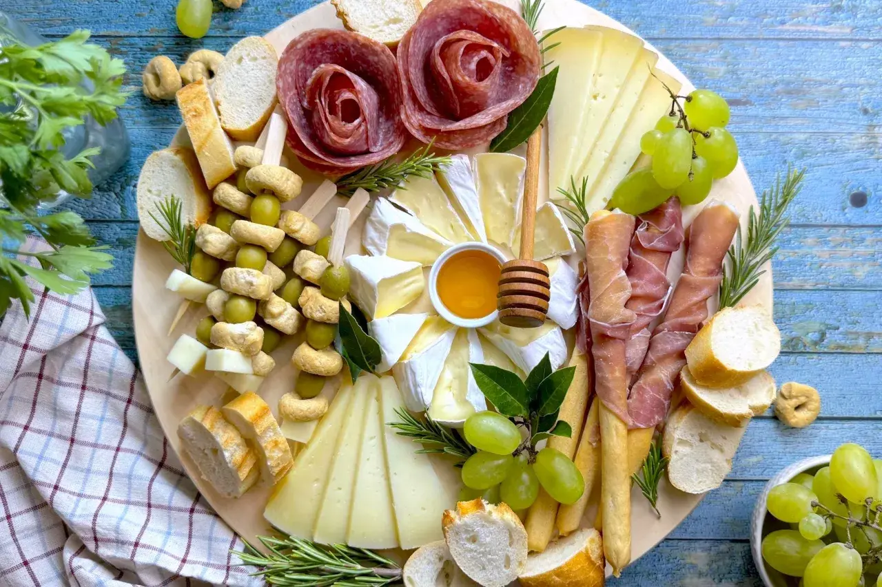Un vassoio con formaggi, salumi a rosa, uva, olive e pane. Ecco come disporre i salumi nel piatto per un antipasto invitante.