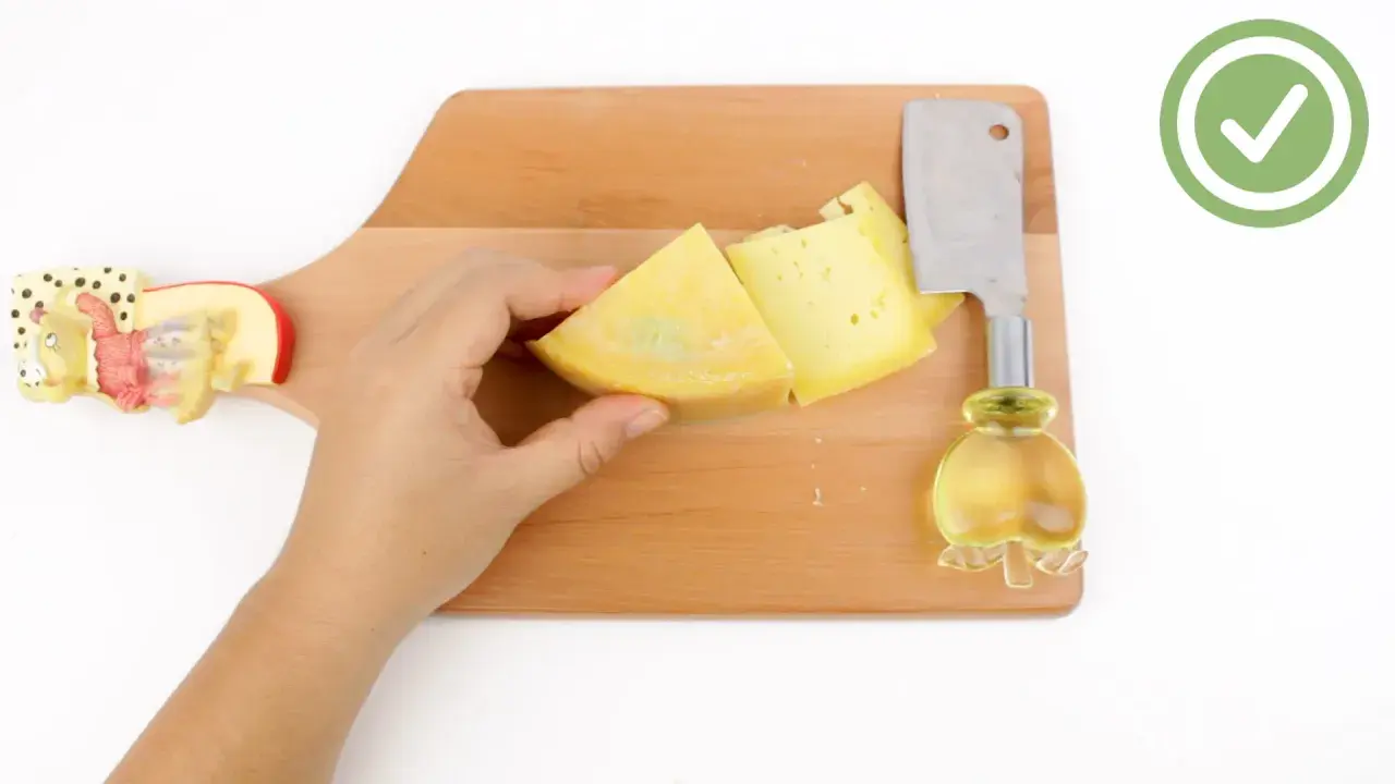 Mano che tiene un pezzo di formaggio giallo su un tagliere di legno, pronto per imparare come tagliare il formaggio a spicchi con un coltello.