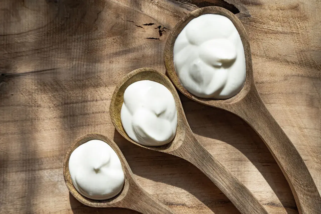 Tre cucchiai di legno pieni di panna da cucina, su un tagliere rustico.