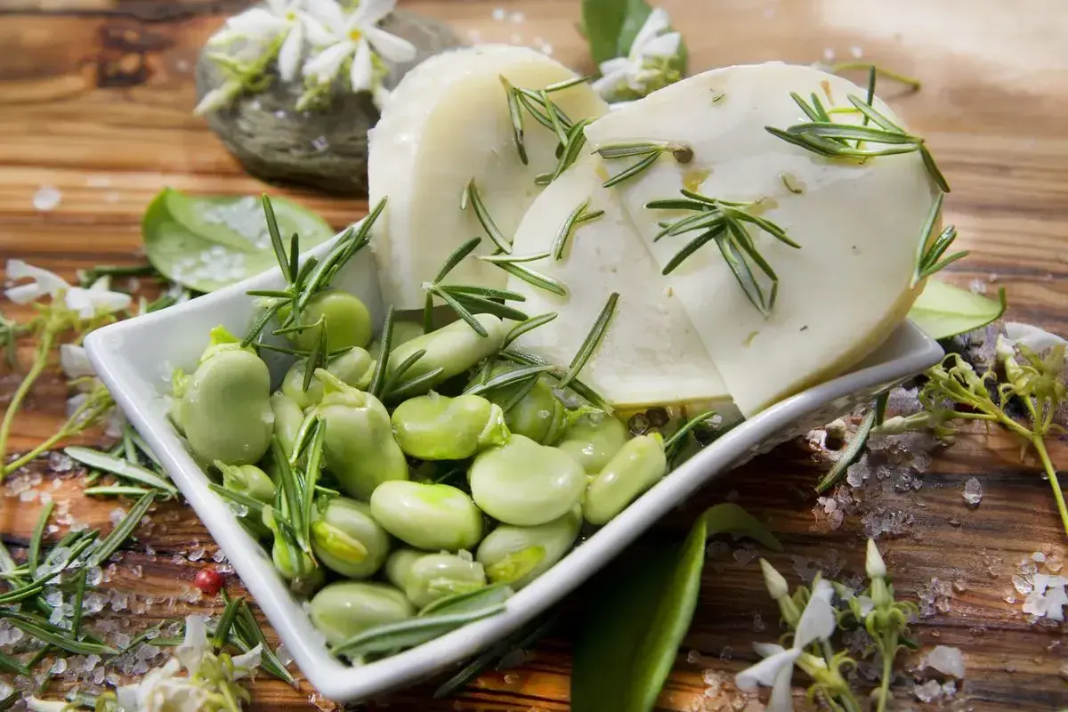 Baccelli freschi e fette di pecorino guarnite con rosmarino su un tagliere di legno.