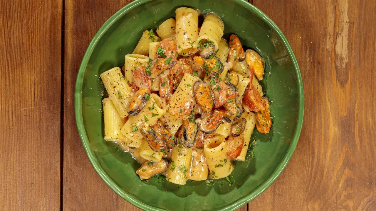 Rigatoni con cozze e pomodorini, conditi con una cremosa salsa al pecorino e prezzemolo fresco.