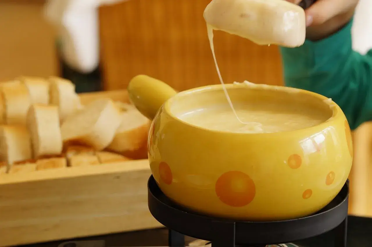 Un pezzo di pane viene intinto in una fonduta di formaggio filante, un modo delizioso per fondere il formaggio.