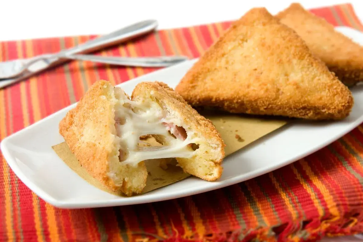 Mozzarella in carrozza dorata e filante, preparata in friggitrice ad aria, servita su un piatto bianco con tovaglietta a righe rosse.