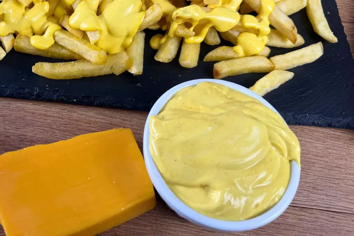 Patatine fritte ricoperte di cremosa salsa cheddar, con un blocco di formaggio e una ciotola di salsa a lato.