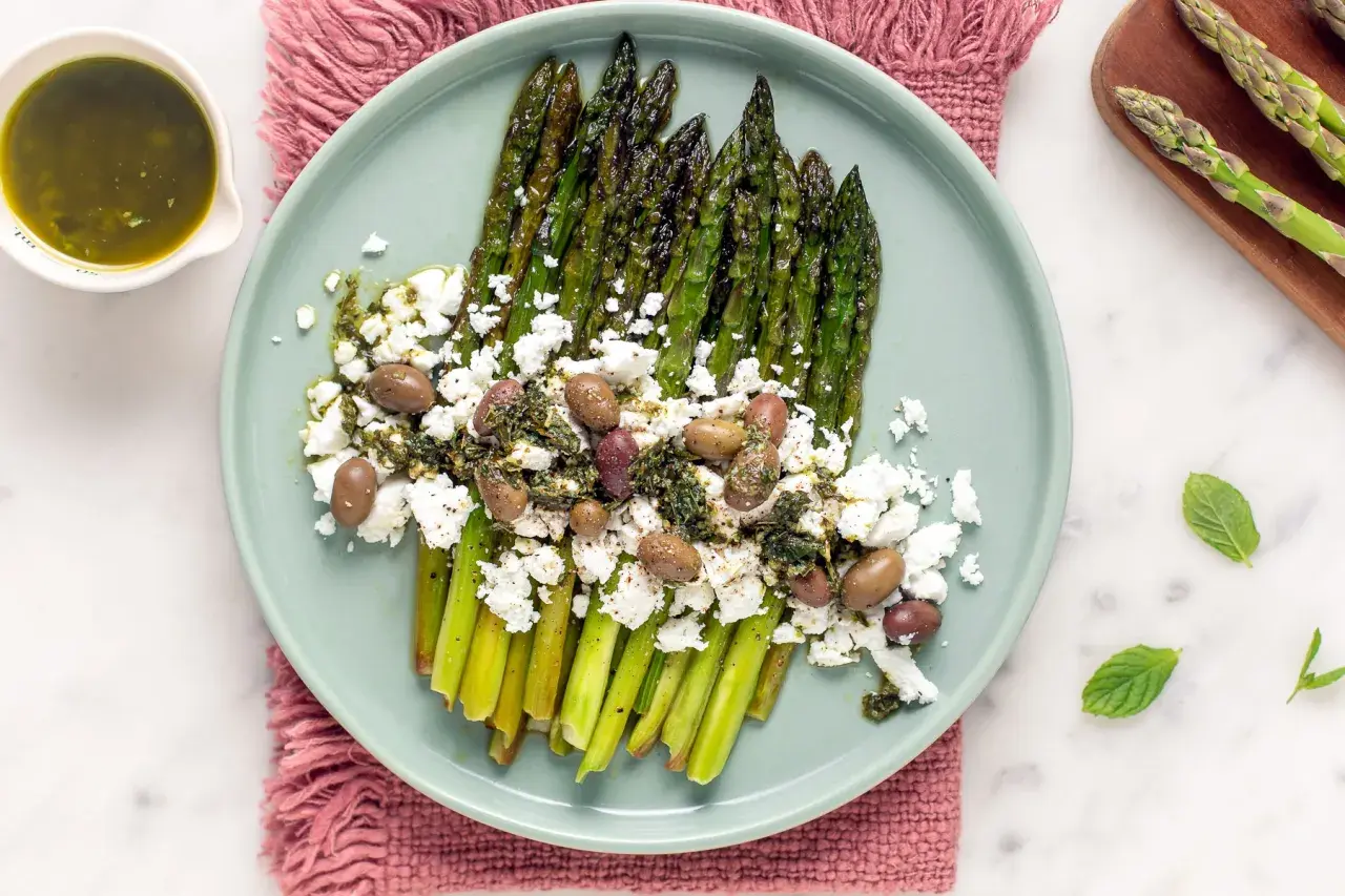 Asparagi grigliati con feta sbriciolata, olive e salsa verde. Un modo gustoso per condire la feta e creare un piatto fresco e saporito.